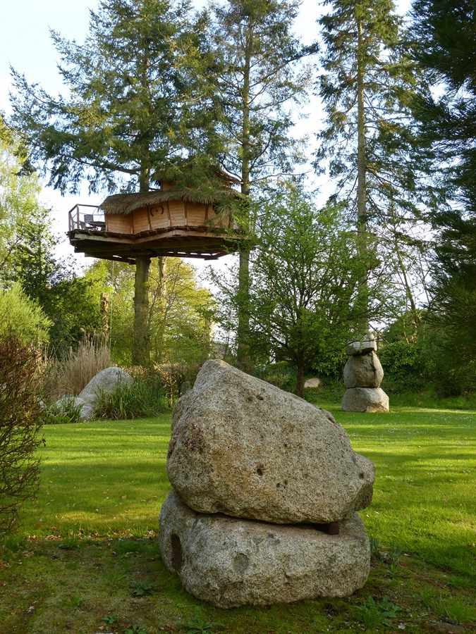 P1070784 (Copier) Cabane perchée dans les arbres en Bretagne, entourée de rochers et de verdure.