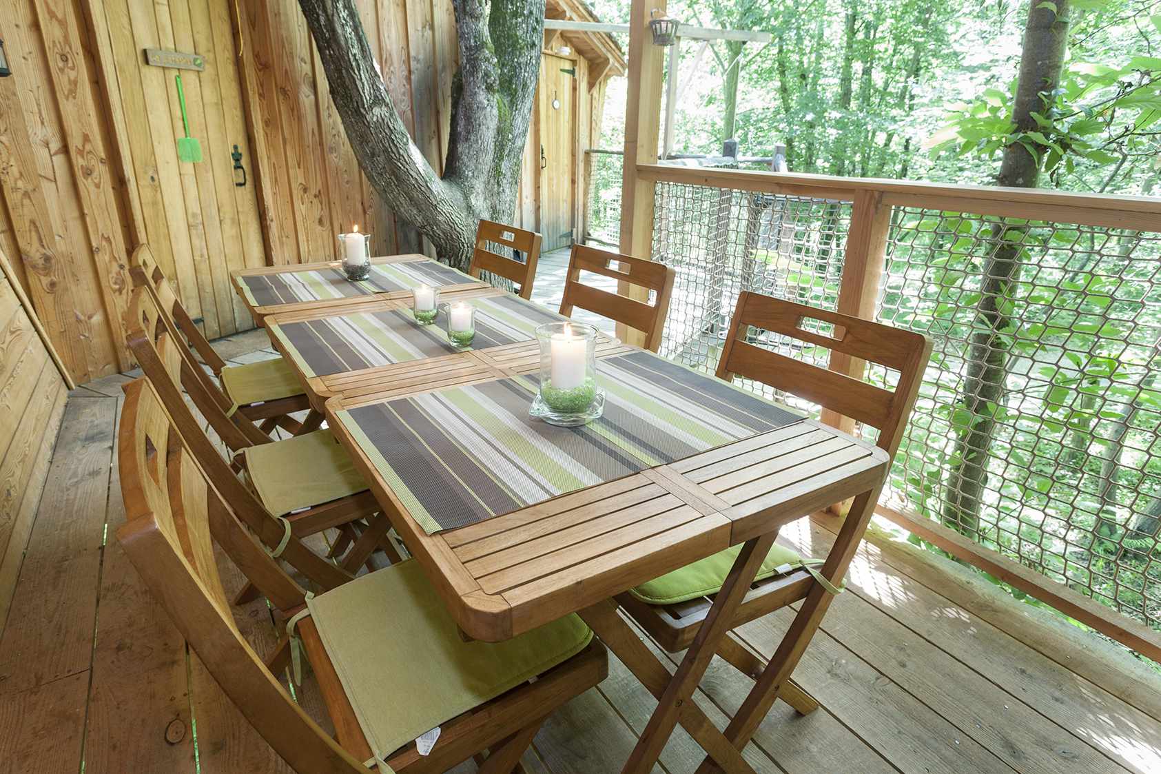 photojp-angei-jp-angei2585 Cabane perchée en bois avec une table en terrasse, entourée darbres verdoyants.