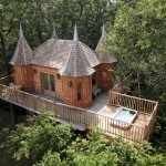 Cabane en bois perchée dans les arbres, avec balustrade et jacuzzi extérieur.
