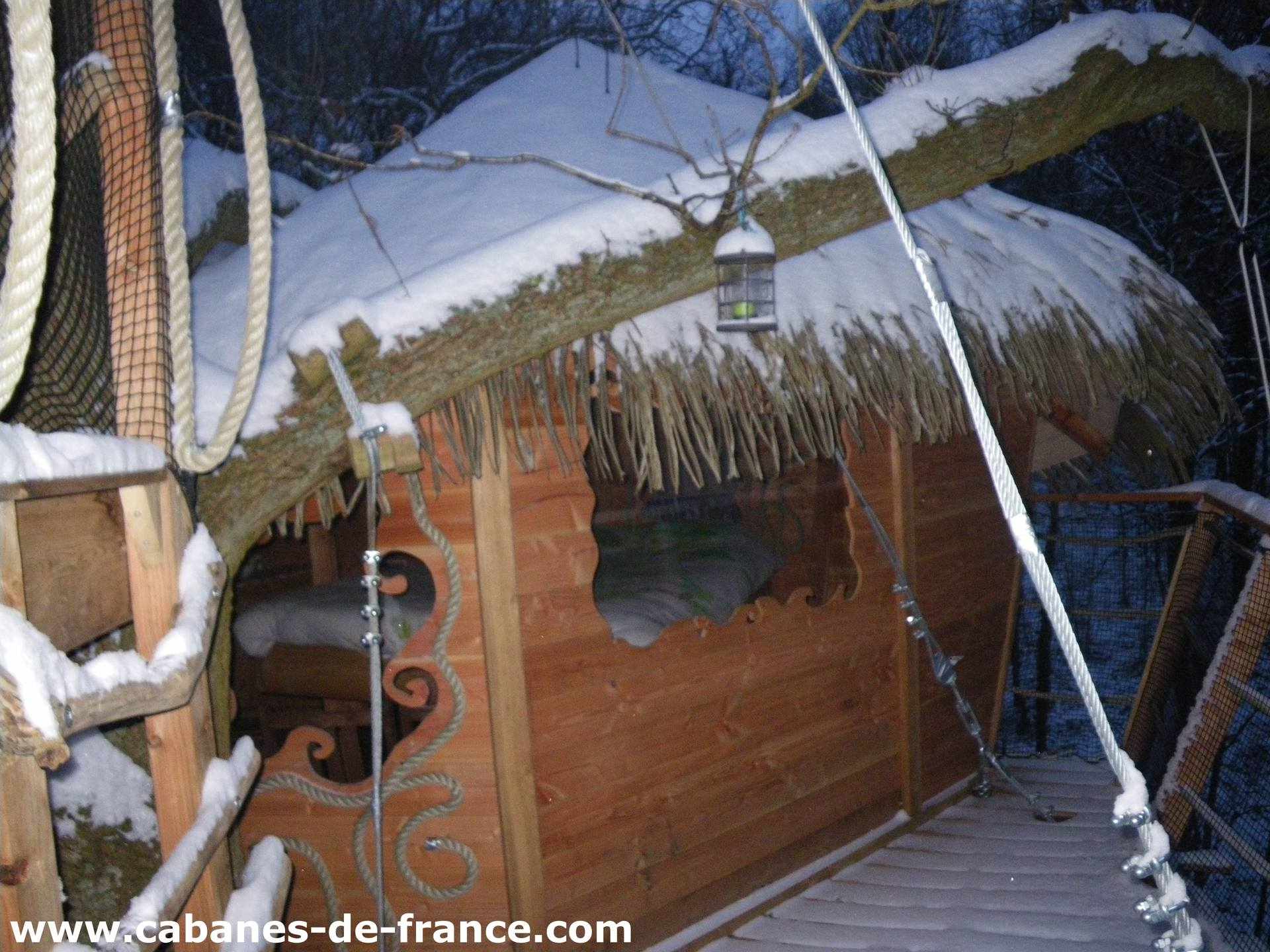IMGP3321_cabanes-de-france Cabane perchée en bois sous la neige, avec un toit en chaume et une vue sur la nature.