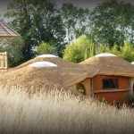 Hébergement insolite : maison en terre avec toit en pente et terrasse en bois.