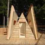 Cabane en bois en forme de tipi, entourée dune terrasse en bois et dun jacuzzi.