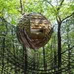 Cabane suspendue dans les arbres, avec un toit en bardeaux et un filet de sécurité.