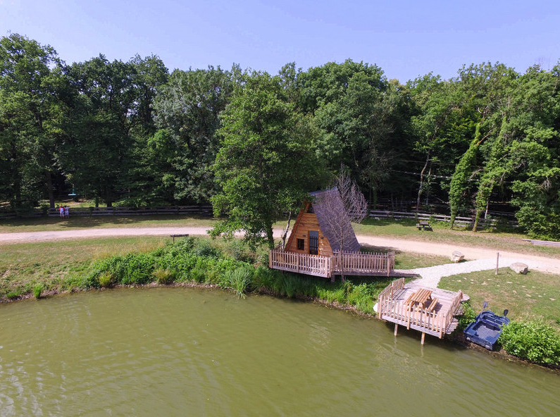 Sans titre1 Cabane en bois au bord dun lac, entourée de verdure en Auvergne-Rhône-Alpes.
