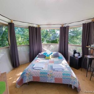 Chambre dans une cabane perchée, avec vue sur la nature et décoration colorée.