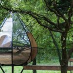 Cabane suspendue moderne, miroir reflétant la verdure environnante.