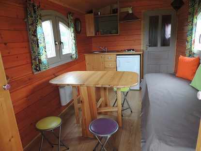 interieur +tablelow Cabane en bois à Limousin, intérieur chaleureux avec table en bois et coussins colorés.