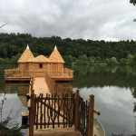 Cabane en bois sur pilotis, entourée dun lac paisible et de verdure.