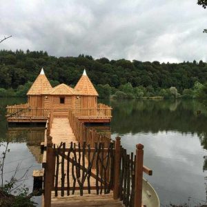 Cabane en bois sur pilotis, entourée dun lac paisible et de verdure.