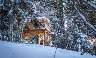 Cabane perchée en bois, entourée de neige et darbres majestueux en Rhône-Alpes.