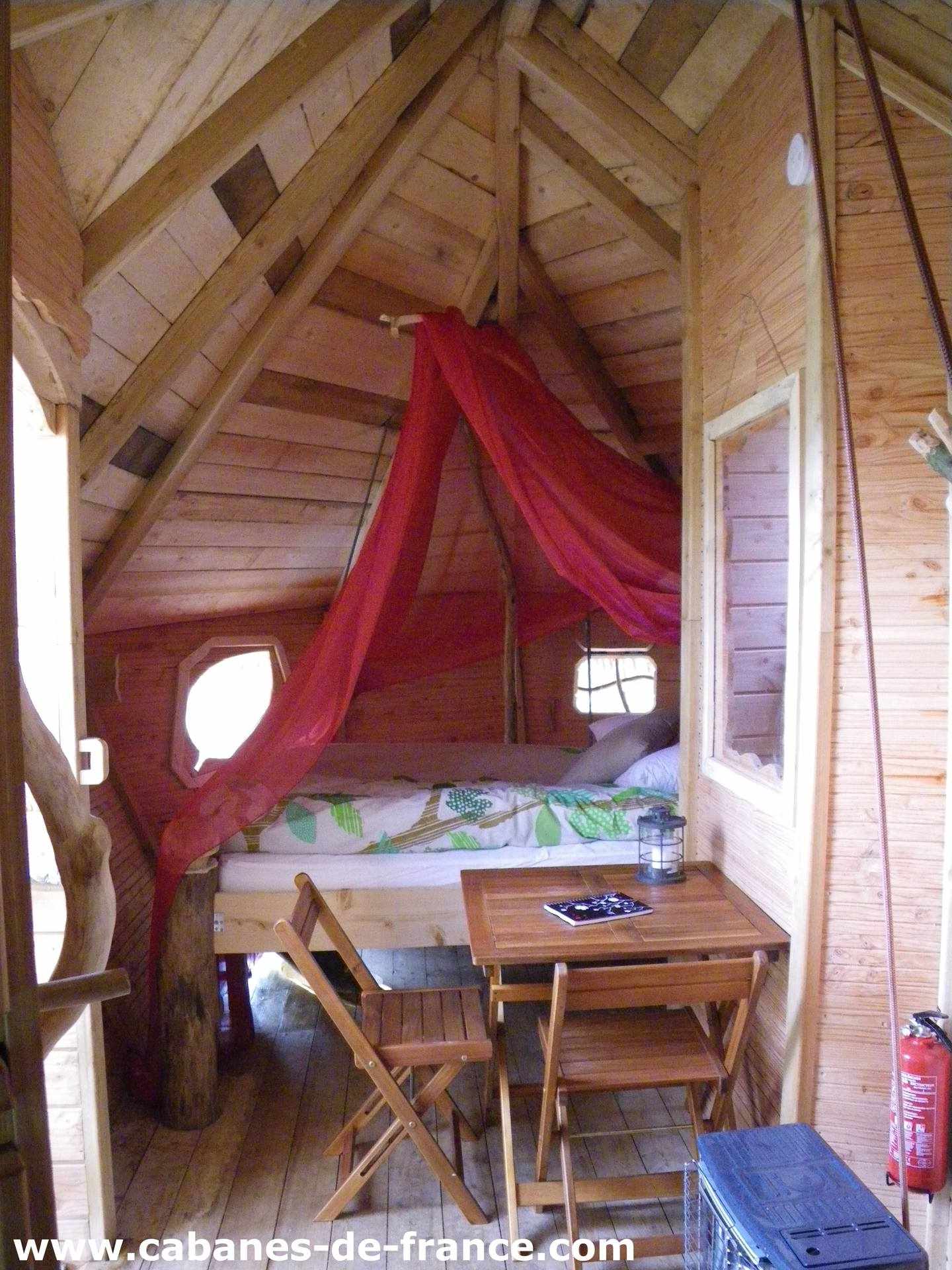 IMGP0705_cabanes-de-france Cabane en bois à Haute-Normandie, avec un lit sous un voile rouge et un coin repas.