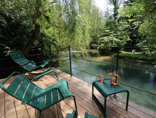 Hébergement insolite en Bourgogne : terrasse en bois avec chaises, vue sur la rivière.