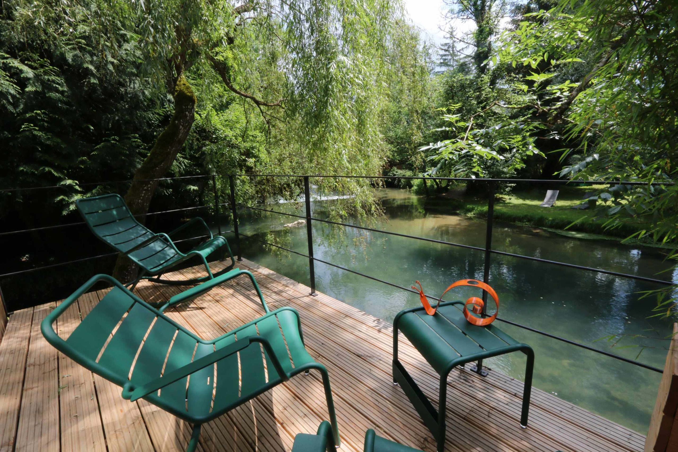 Hébergement insolite en Bourgogne : terrasse en bois avec chaises, vue sur la rivière.