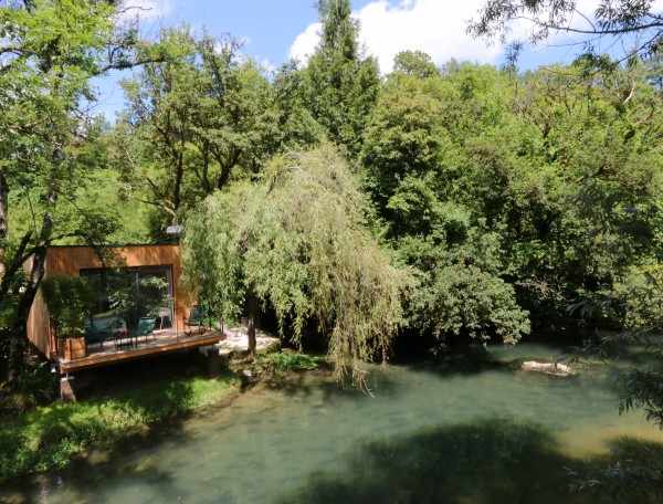 Cabane en bois au bord dune rivière, entourée de verdure luxuriante en Bourgogne.