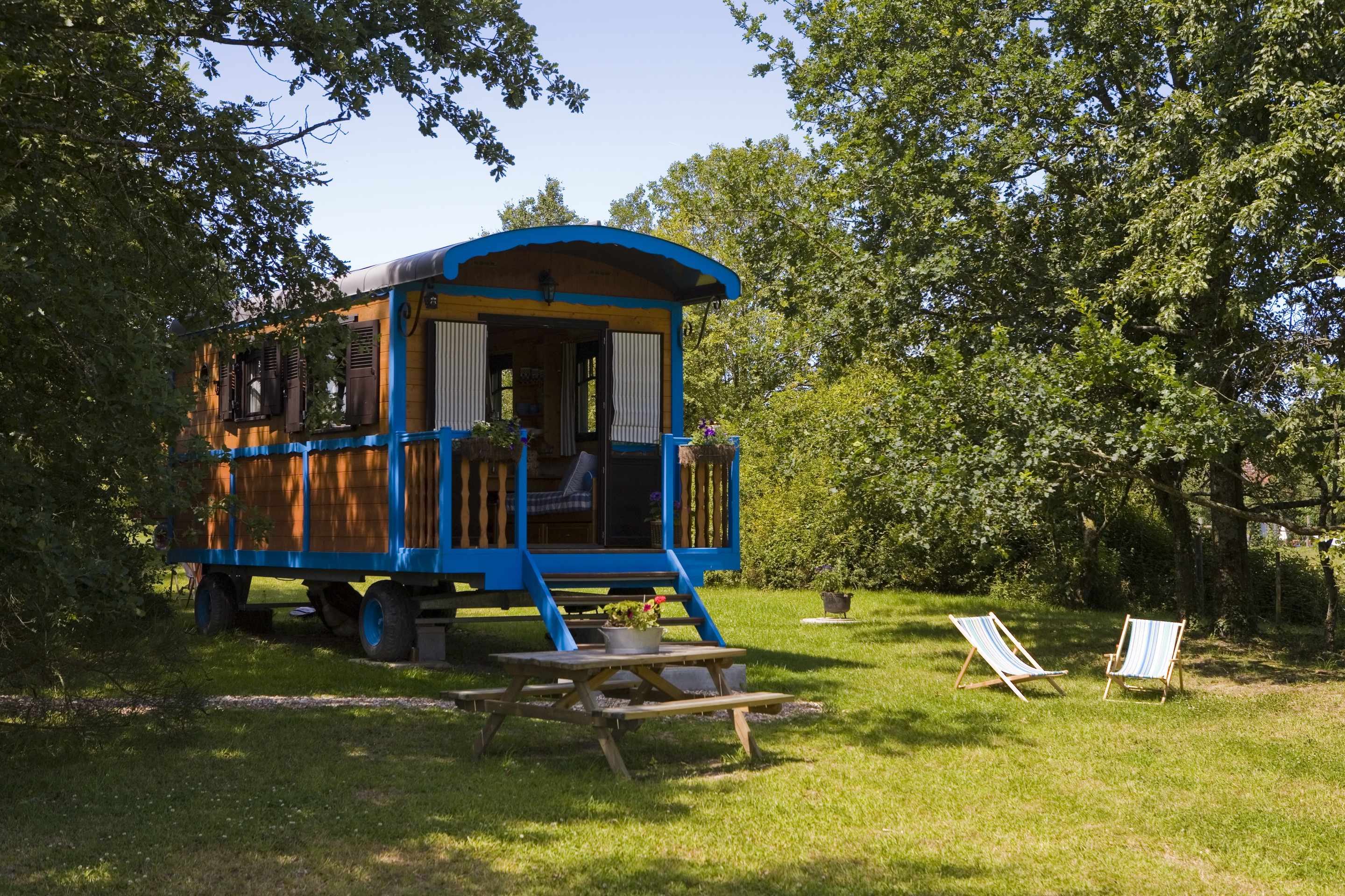 Charmante roulotte colorée avec terrasse, entourée dun jardin verdoyant.