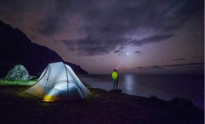 Camping en bord de mer, tente illuminée sous un ciel étoilé.