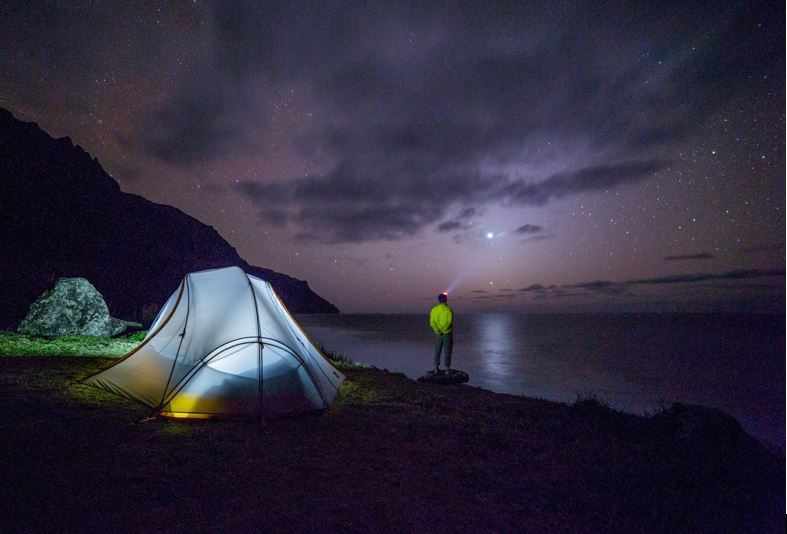 Camping en bord de mer, tente illuminée sous un ciel étoilé.