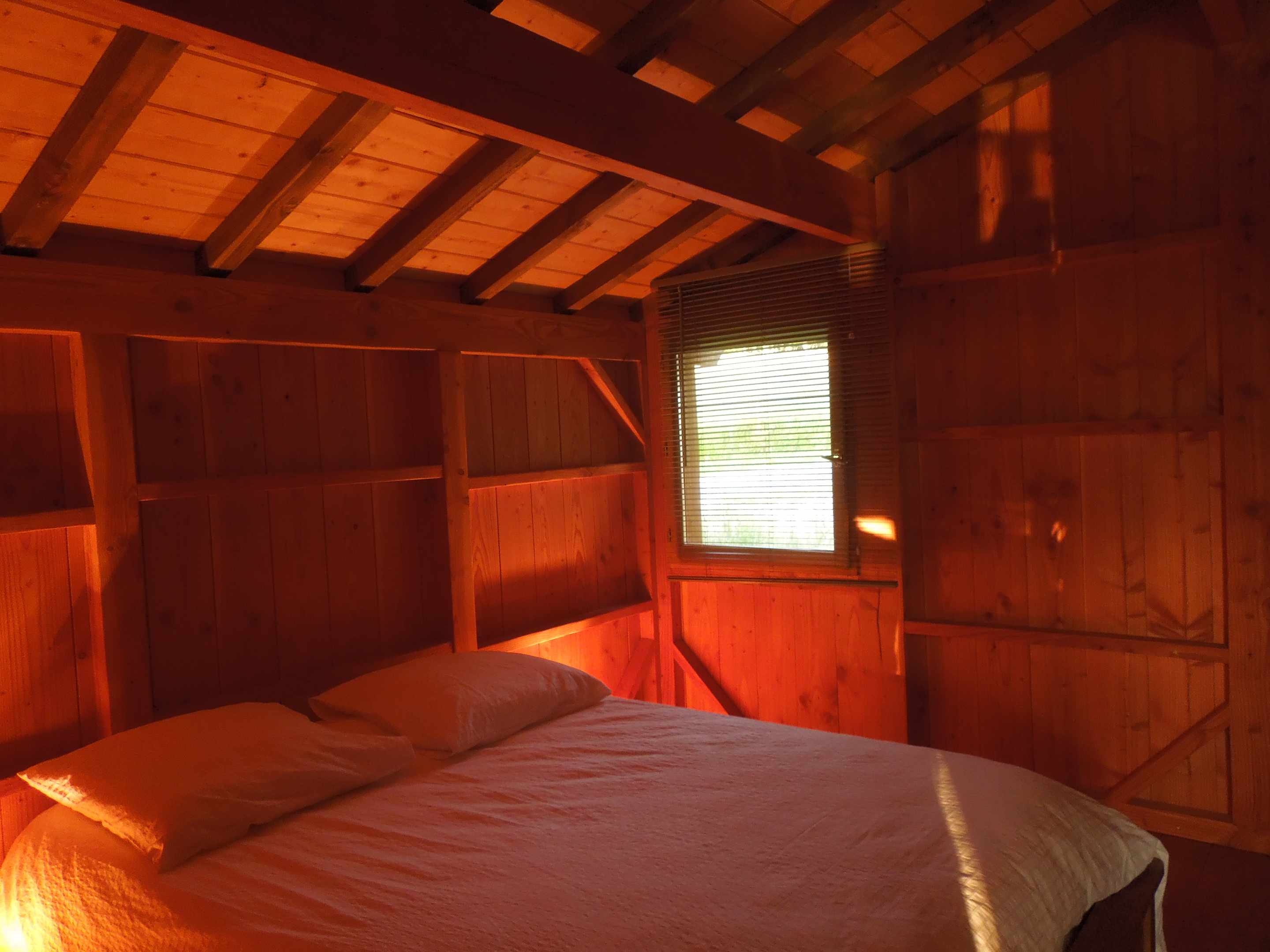pb_08 Chalet en bois chaleureux avec lit double et lumière douce filtrant par la fenêtre.
