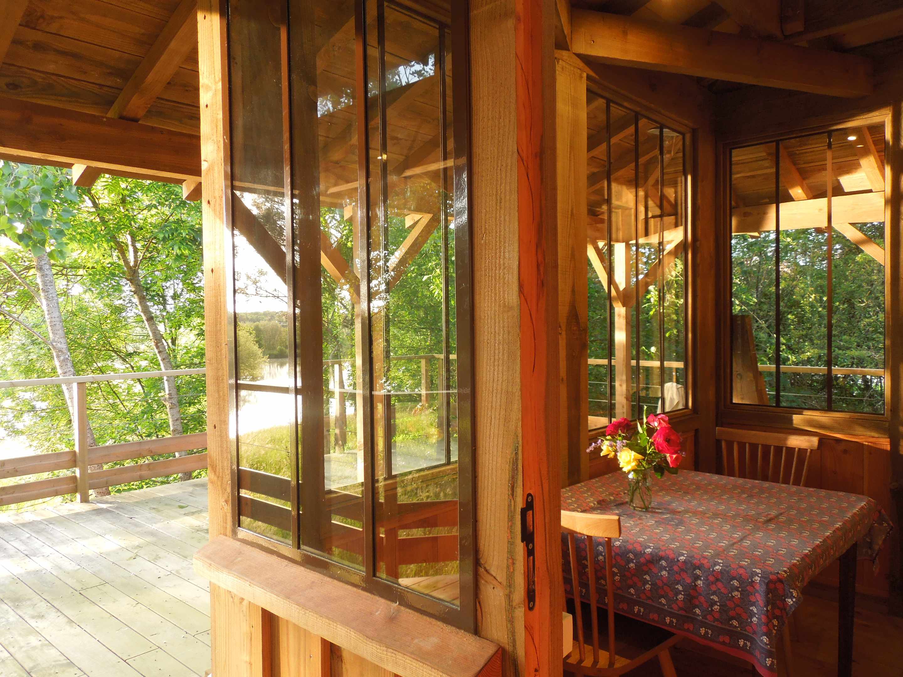 pb_09 Cabane en bois avec grandes fenêtres, vue sur la nature et une table décorée de fleurs.