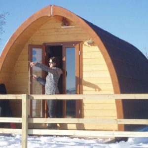 Cabane en bois avec un toit arrondi, située dans un paysage enneigé.