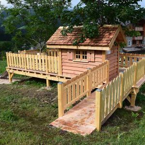 Cabane en bois sur pilotis, entourée de verdure et dune terrasse en bois.