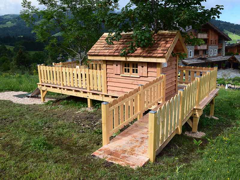 Cabane en bois sur pilotis, entourée de verdure et dune terrasse en bois.