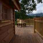 Cabane en bois avec terrasse ensoleillée et vue sur les montagnes verdoyantes.