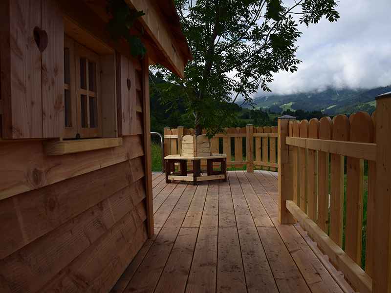 Cabane en bois avec terrasse ensoleillée et vue sur les montagnes verdoyantes.