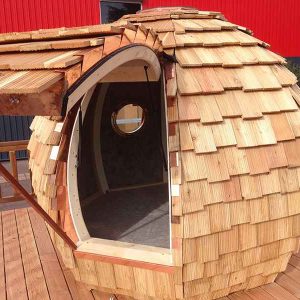 Cabane en bois en forme de bulle avec un toit en bardeaux et une porte ronde.