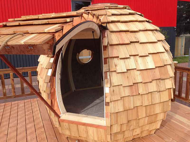 Cabane en bois en forme de bulle avec un toit en bardeaux et une porte ronde.