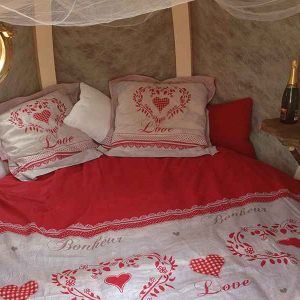 Hébergement romantique en forme de bulle, lit douillet avec draps rouges et champagne.
