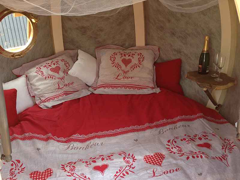Hébergement romantique en forme de bulle, lit douillet avec draps rouges et champagne.