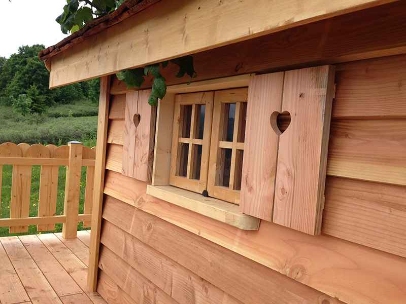 Cabane en bois avec fenêtres à cœurs et terrasse en bois. Ambiance chaleureuse et naturelle.