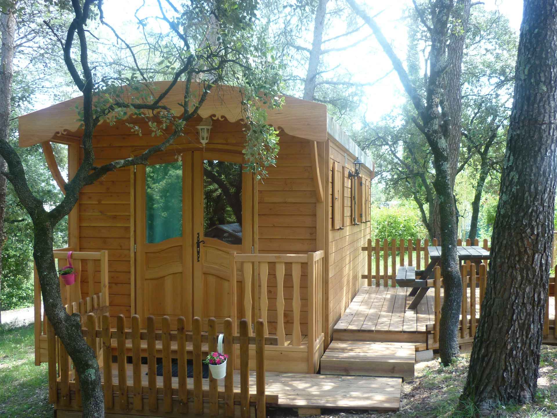 P1060297 Cabane en bois nichée dans les arbres, avec terrasse en bois et jardin verdoyant.