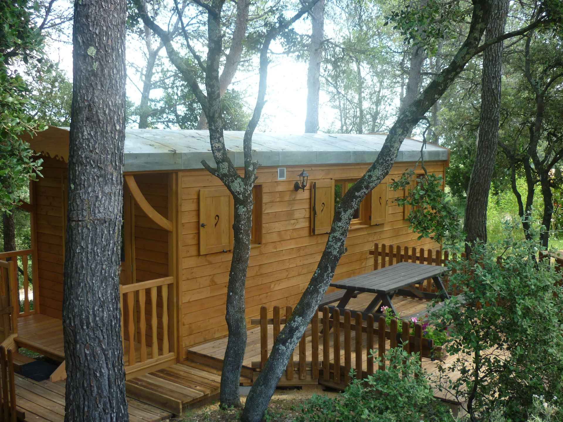 P1060299 Cabane en bois entourée darbres, avec terrasse et table extérieure.