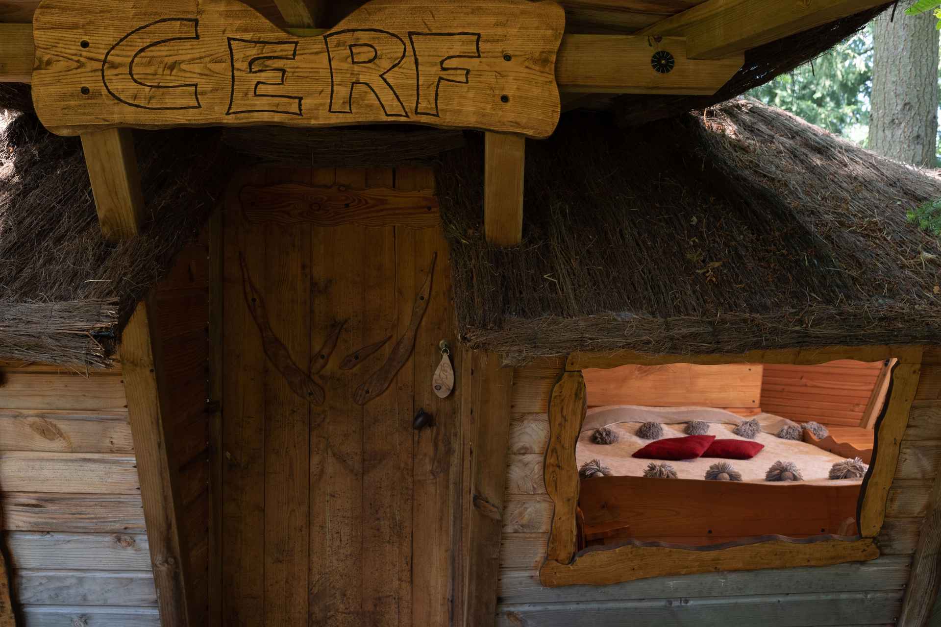 version-internet-29 cerf Cabane en bois avec toit de chaume, lit douillet visible à travers la fenêtre.