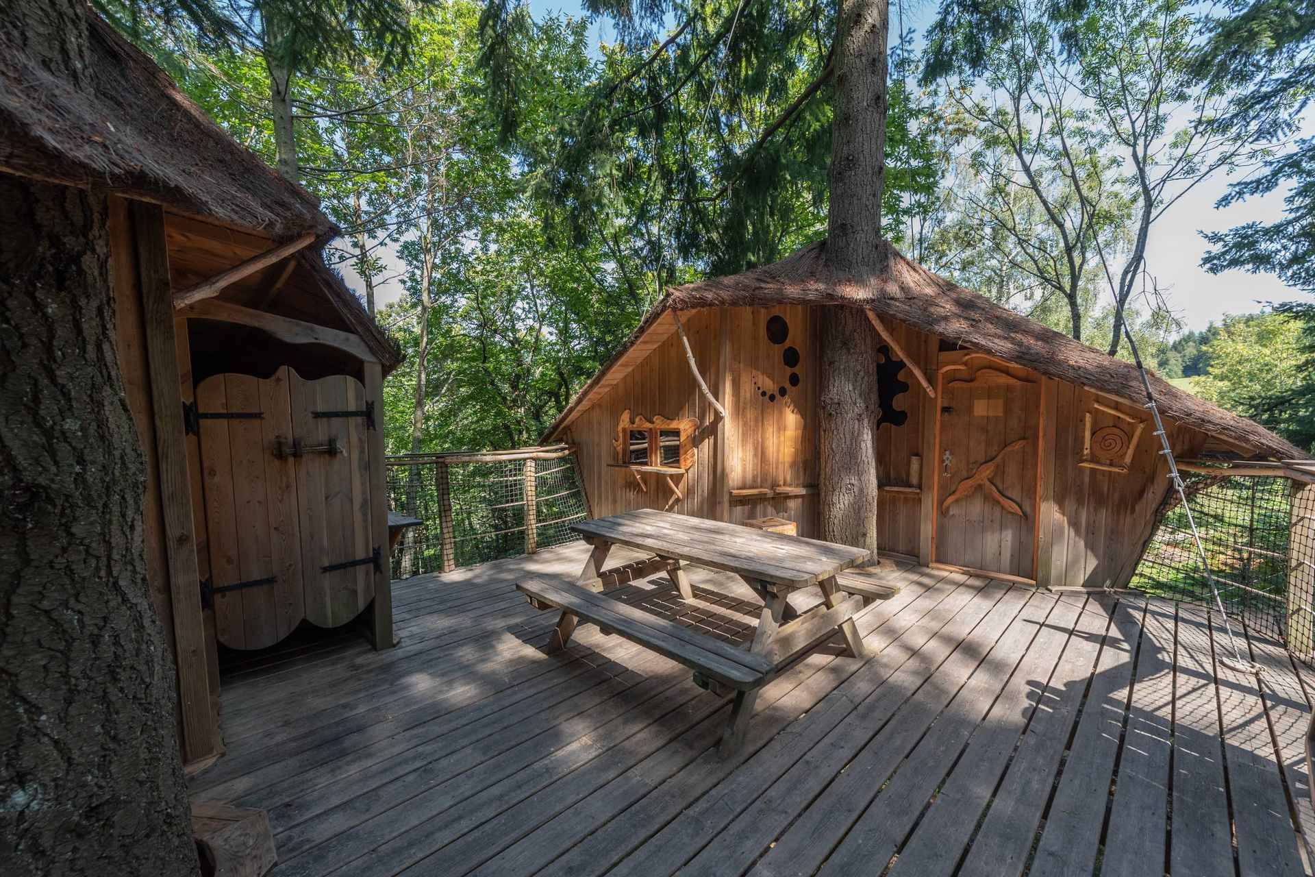 version-internet-43 castor Cabane en bois perchée, entourée darbres, avec une terrasse en bois accueillante.