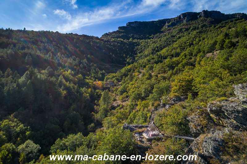 DJI_0513_resultat Cabane perchée dans les arbres, entourée de verdure et de montagnes majestueuses.