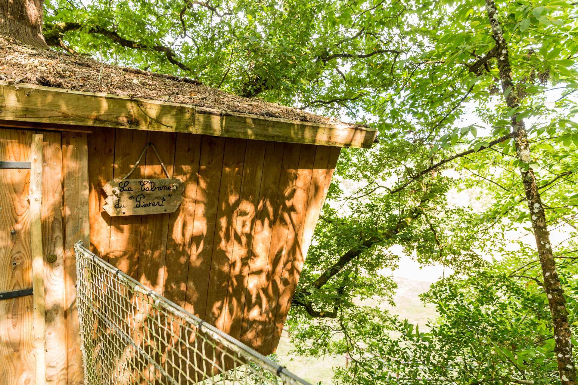 Cabane perchée dans les arbres, entourée de verdure, avec un toit en bois.