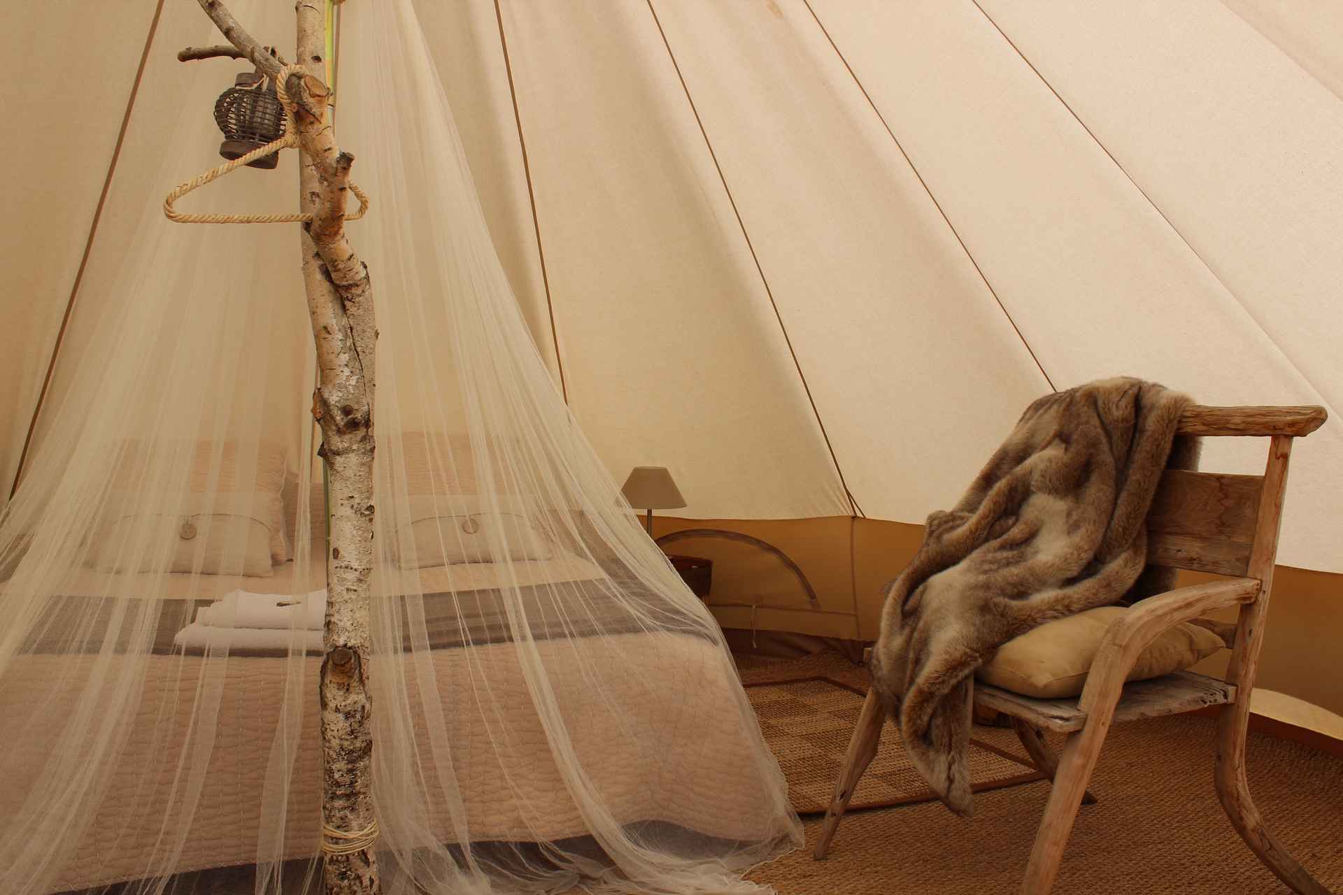 22 Tente glamping en Auvergne-Rhône-Alpes, avec lit douillet et fauteuil en bois.