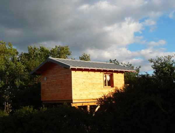 Cabane en bois perchée, entourée de verdure sous un ciel nuageux en Auvergne-Rhône-Alpes.