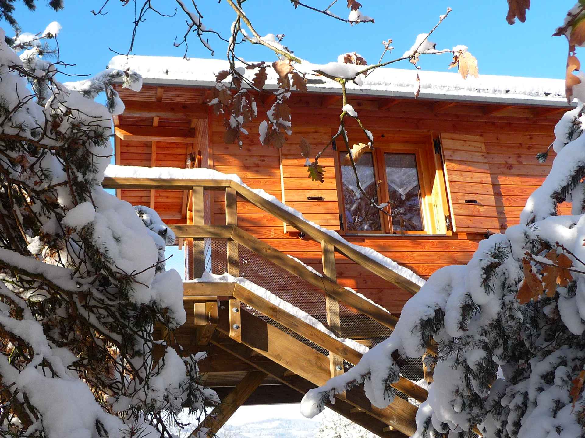 Cabane en bois perchée, entourée de neige et de branches enneigées.