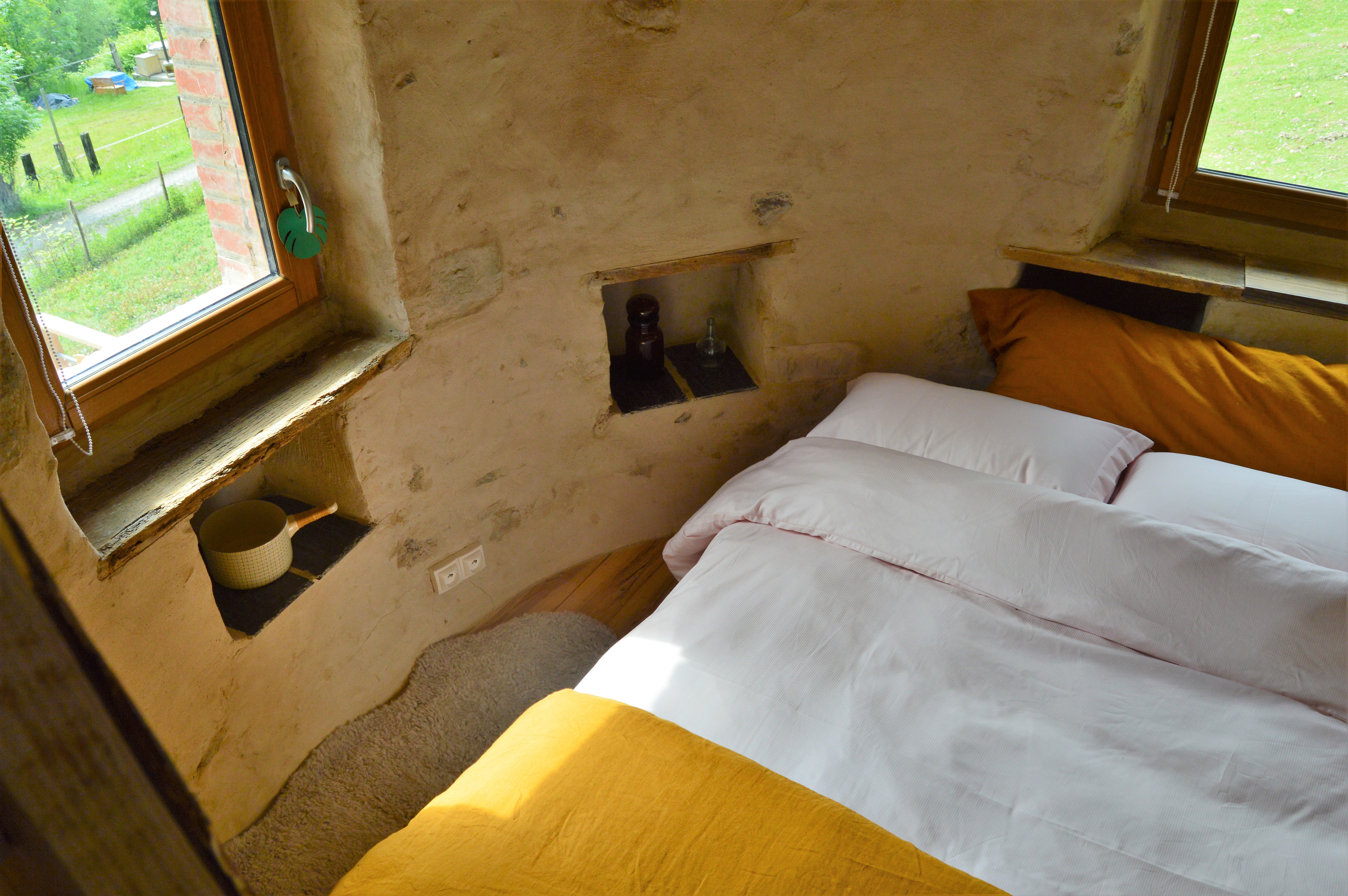 DSC_0299 Chambre cosy en éco-hébergement, murs en pierre et vue sur la nature verdoyante.