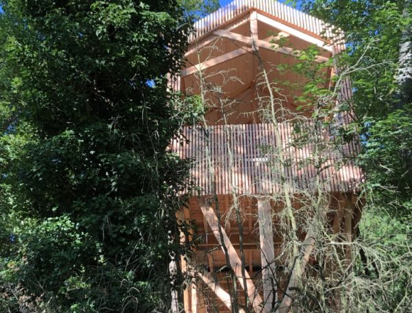 Cabane perchée en bois, entourée de verdure, offrant une vue imprenable sur la nature.