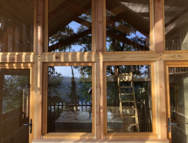 Cabane en bois avec grandes fenêtres, offrant une vue sur la nature environnante.