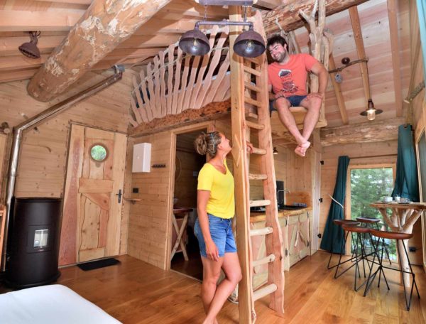 Cabane en bois perchée avec échelle, ambiance chaleureuse et naturelle.