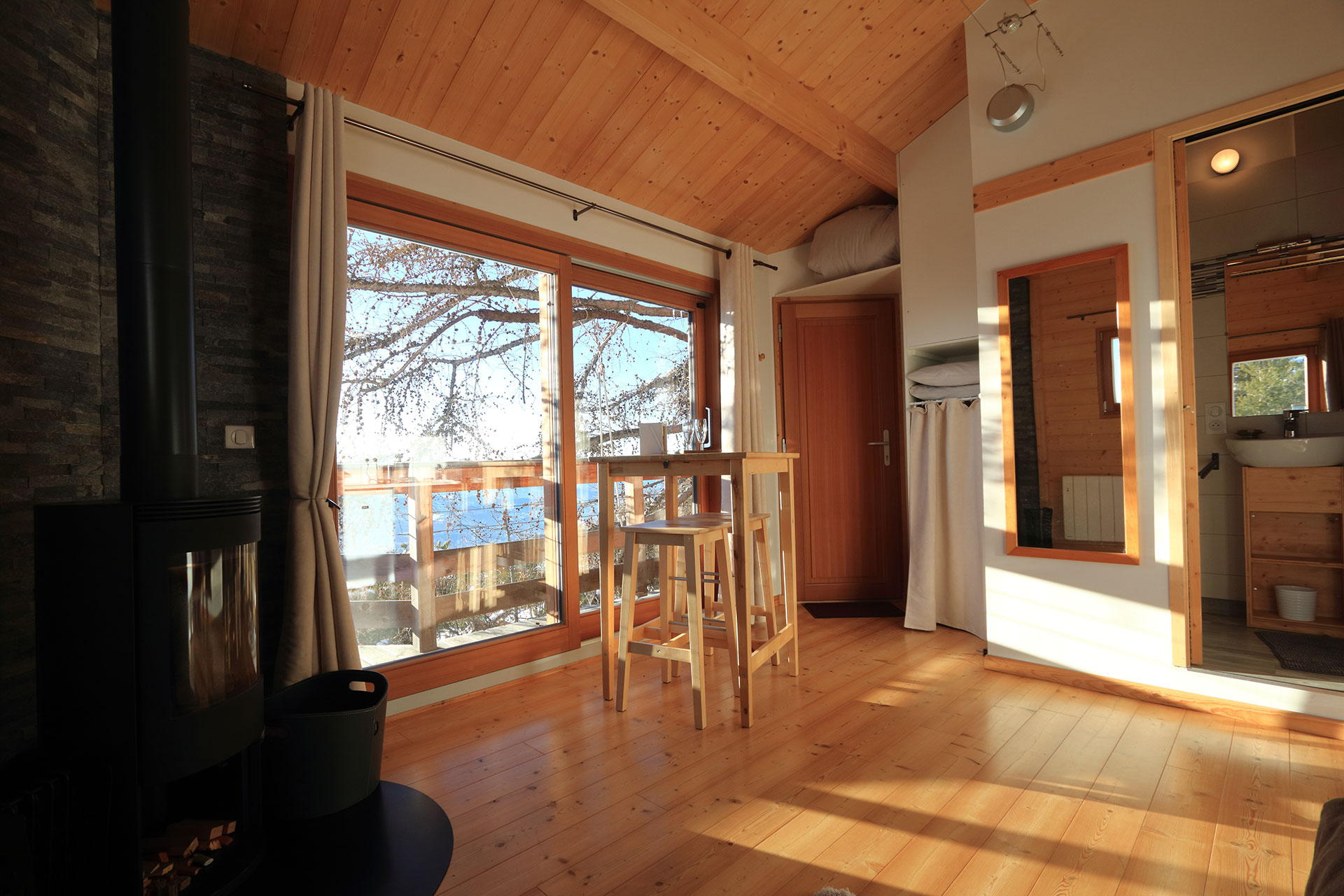 Cabane en bois lumineuse avec vue sur le lac et poêle à bois chaleureux.