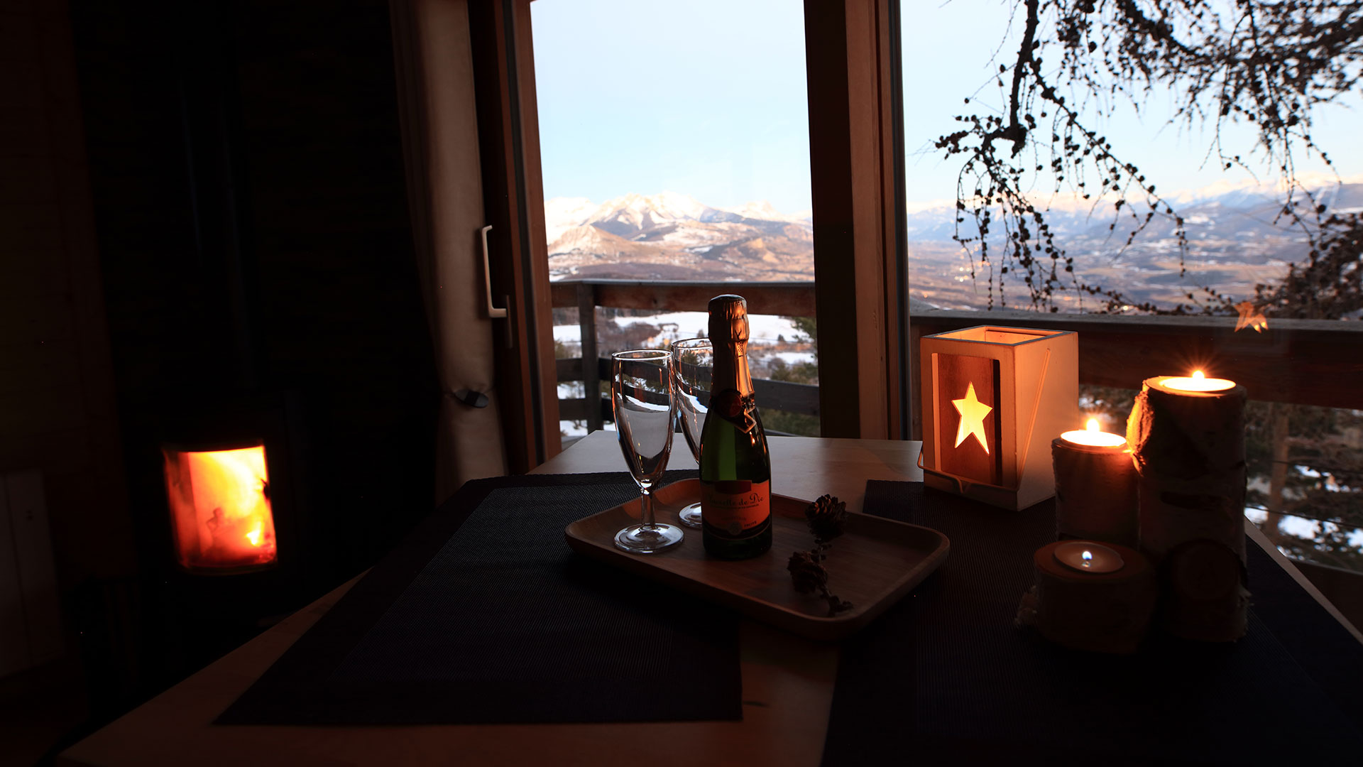 Cabane en bois avec vue sur les montagnes, champagne et bougies créent une ambiance romantique.