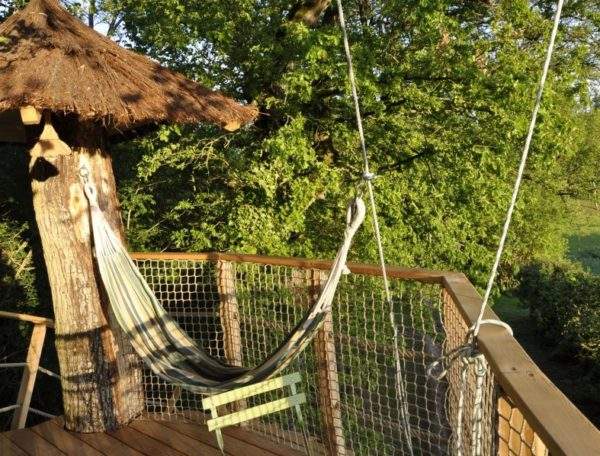 Cabane perchée avec hamac, entourée de verdure luxuriante au Centre.