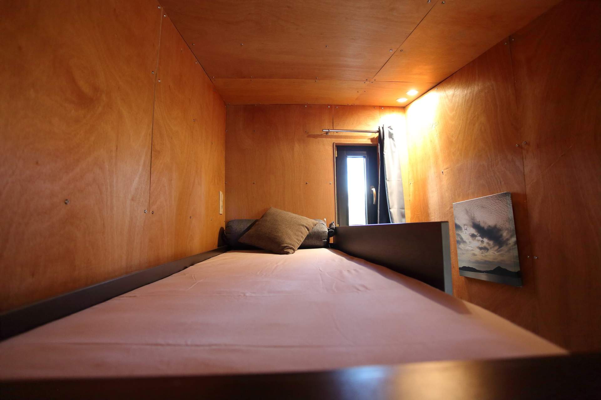 IMG_5786 Cabane en bois cosy avec lit simple et fenêtre laissant entrer la lumière.